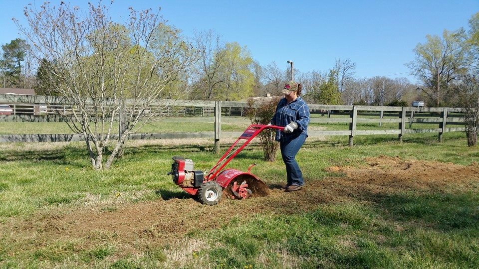 Girl in blue plaid shirt tilling a new garden with a red Troybuilt rototiller.