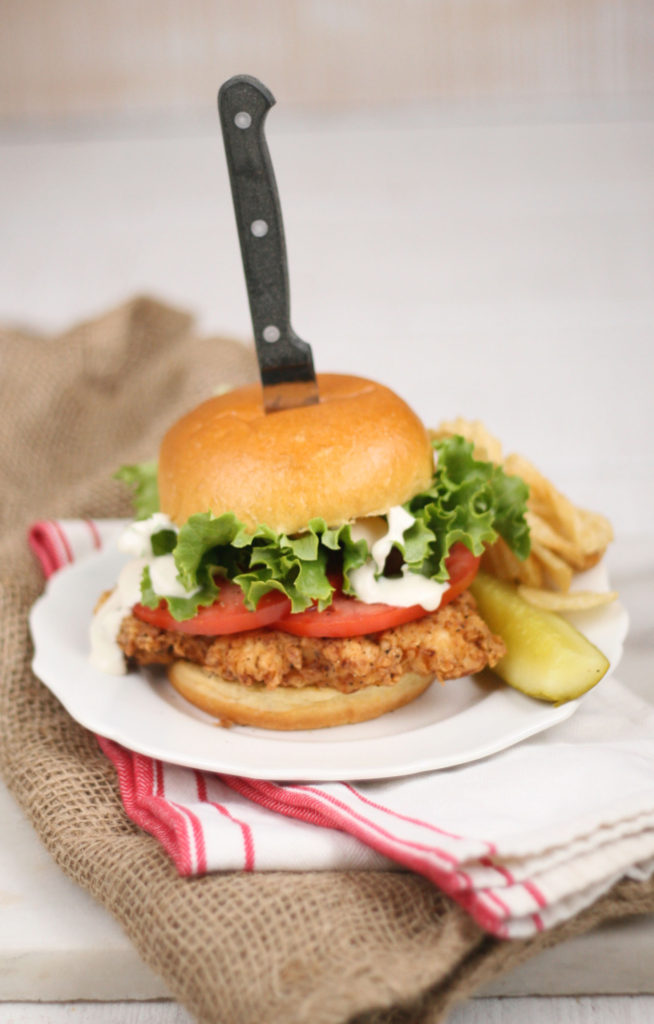 Southern style Buttermilk Fried Chicken Sandwich on a brioche bun, slices of tomatoes, green leaf lettuce, and buttermilk dressing.