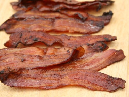 Pieces of maple pepper bacon sitting on wooden cutting board