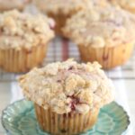 Raspberry Streusel muffin sitting on an aqua floral plate with remainder of muffins cooling in the background on a baking rack.