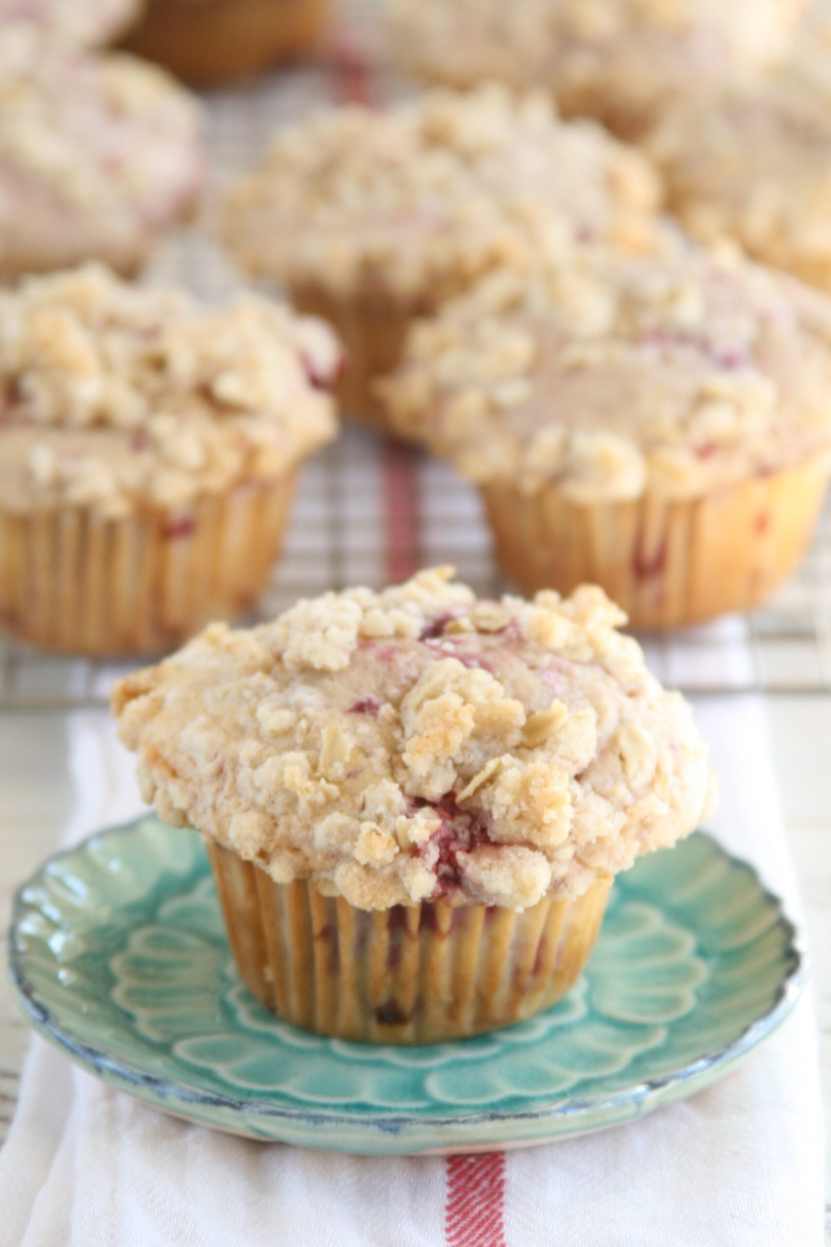 Raspberry Streusel muffin sitting on an aqua floral plate with remainder of muffins cooling in the background on a baking rack.