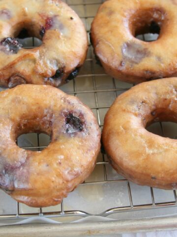 blueberry cake doughnuts with glaze drying on baking rack
