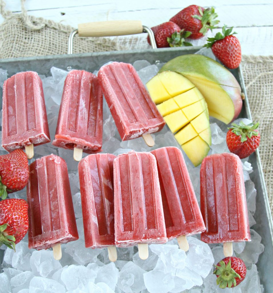 Homemade strawberry mango ice pops sitting in galvanized tray of ice cubes and fresh strawberries surrounding them