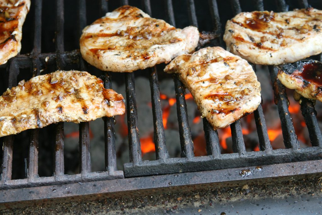 grilled pork chops on the charcoal grill with red hot coals under grates