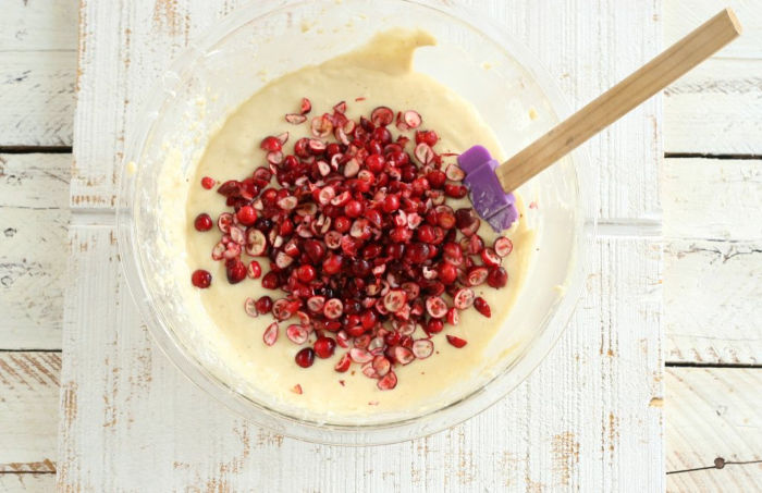 clear glass bowl with muffin batter, rubber spatula folding in fresh chopped cranberries