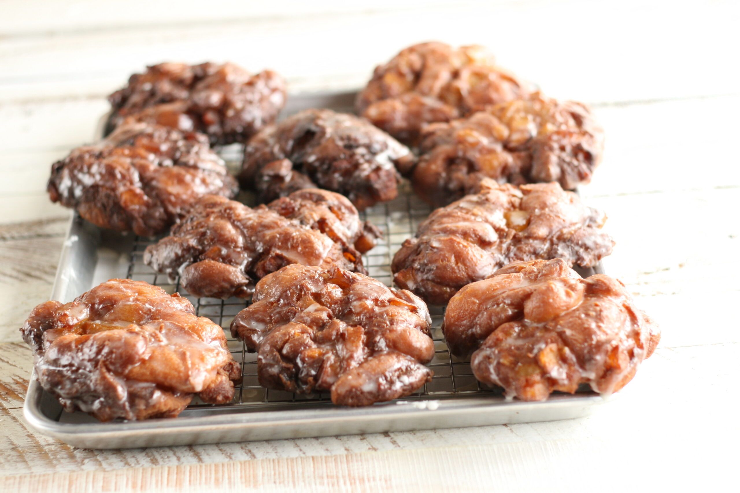 Apple Fritters with a glaze sitting on a sheet pan and baking rack.