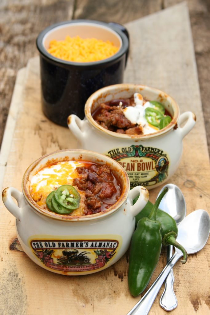 Homemade chili in little crock pots with shredded cheese and pieces of jalapeno peppers