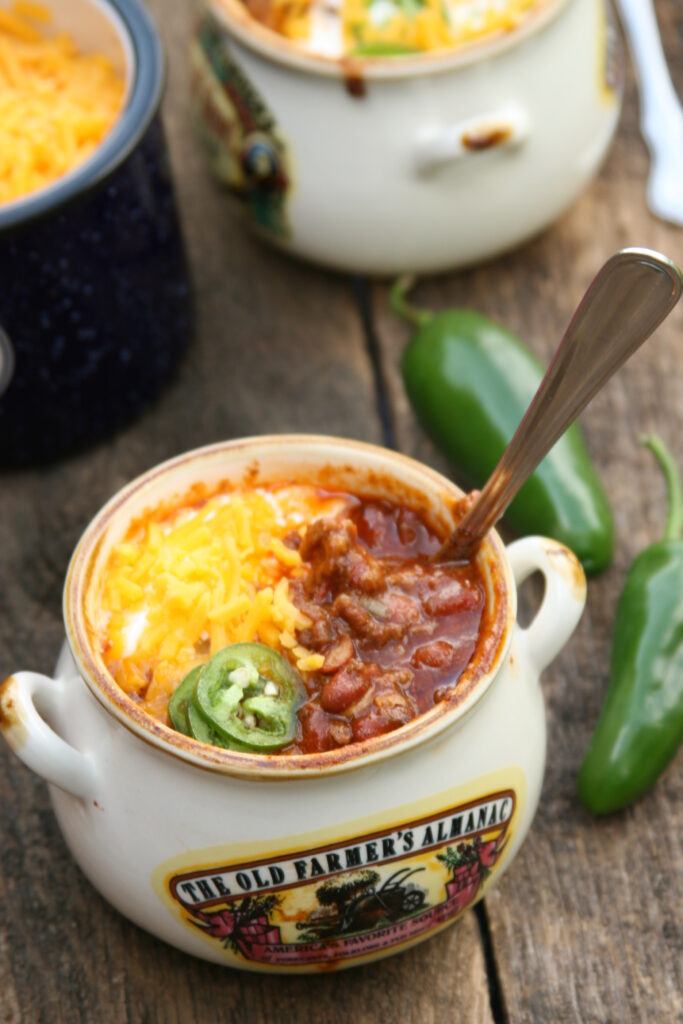 Homemade chili in little bowls with shredded cheddar cheese, sour cream, and jalapeno slices