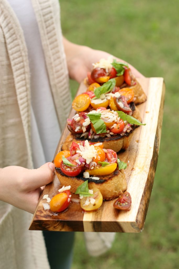 homemade bruschetta on a wooden cutting board with pieces of fresh basil