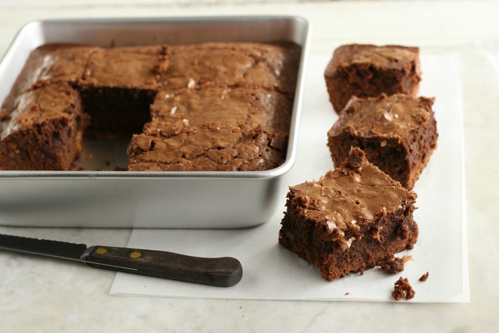 Fudge brownies in a square baking pan and brownies cut sitting on the side with a small knife