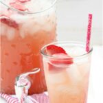 clear glass filled with strawberry lemonade, slice of fresh strawberry in glass, red & white striped paper straw