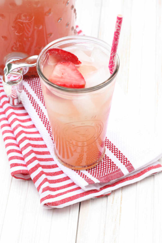 strawberry rhubarb lemonade in a clear glass with slices of strawberries, pink paper straw in the glass