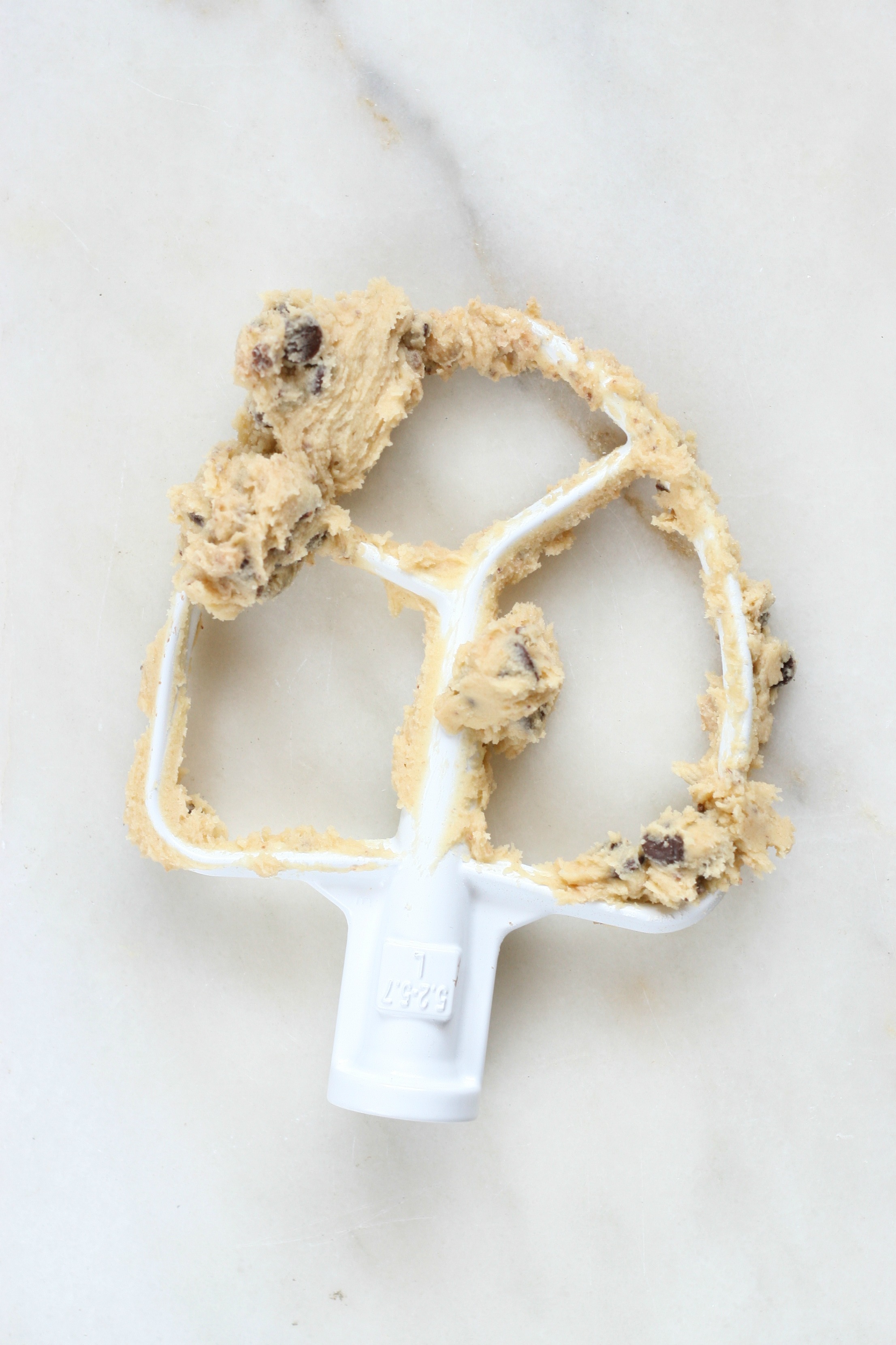 Chocolate chip cookie dough on Kitchenaid beater, sitting on white marble.