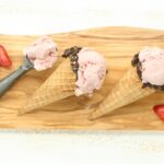 Homemade strawberry ice cream in store bought waffle cones with edges dipped in chocolate and crushed Oreo cookies
