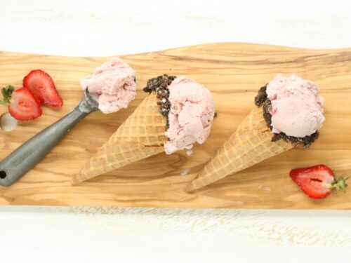 Homemade strawberry ice cream in store bought waffle cones with edges dipped in chocolate and crushed Oreo cookies