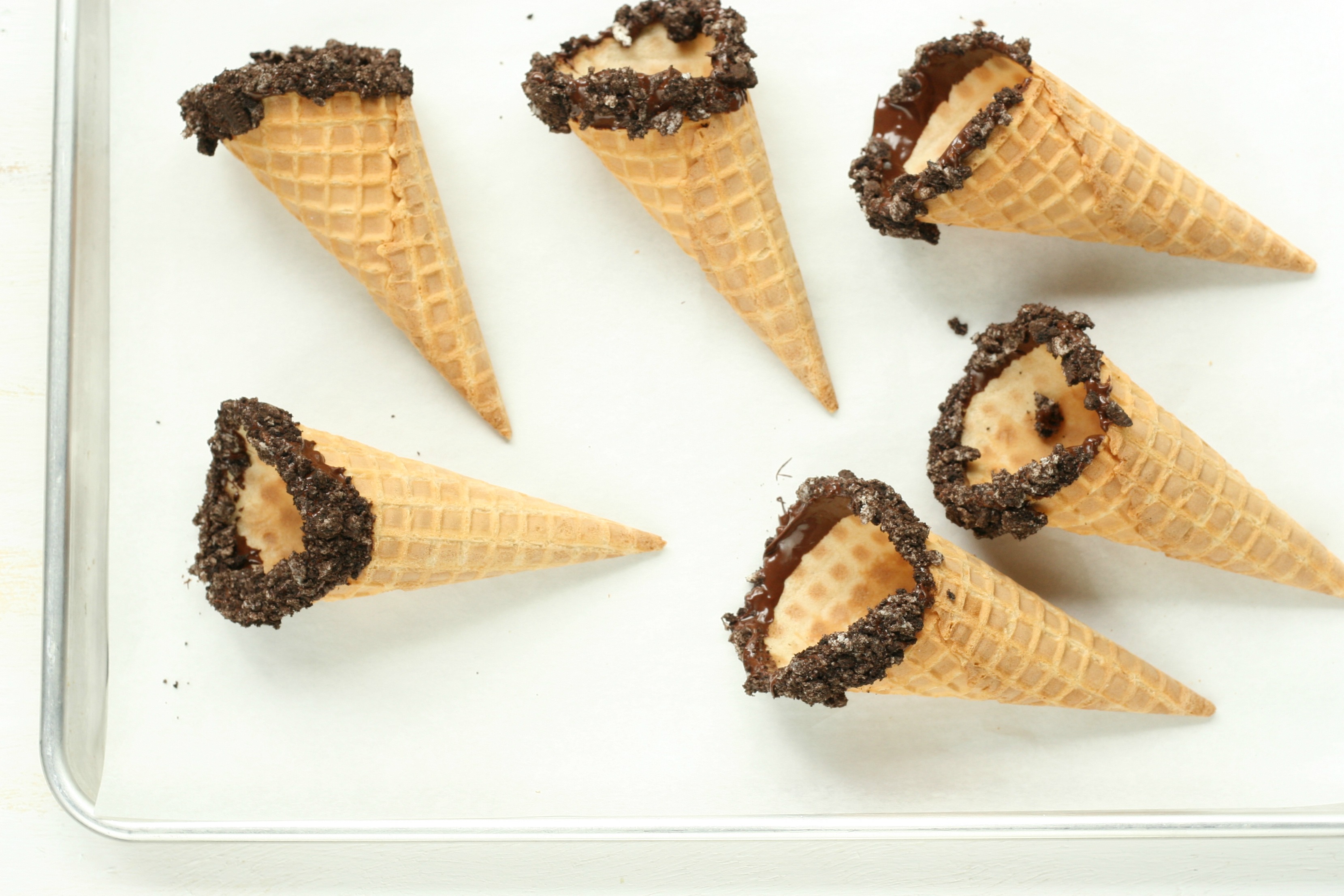 sheet pan of store bought waffle cones dipped in chocolate and rolled in crushed Oreo cookie crumbs.