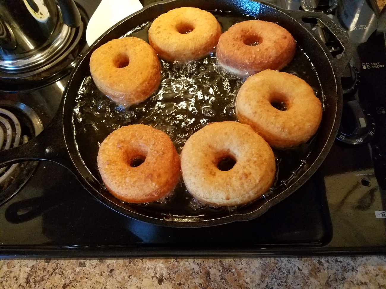 homemade doughnuts being fried up in a cast iron skillet.