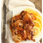 Citrus marinated chicken thighs on a white plate and fork and knife to the left side. Sitting on natural linen and burlap