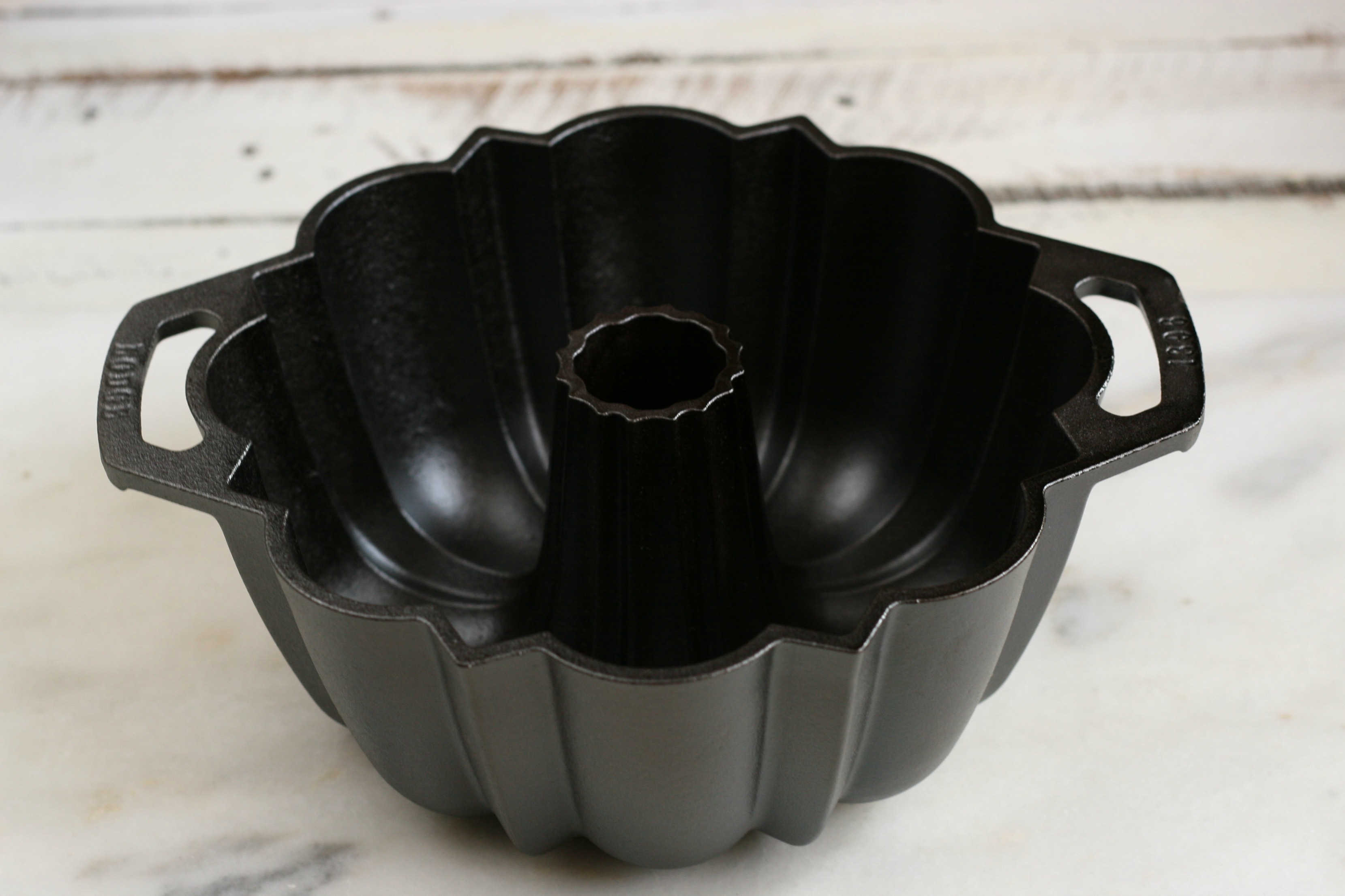 Lodge cast iron fluted cake pan with two handles, on a piece of white marble.
