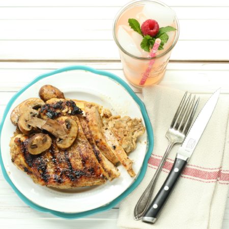 maple whiskey grilled chicken with sauteed mushrooms on a white plate and glass of pink lemonade