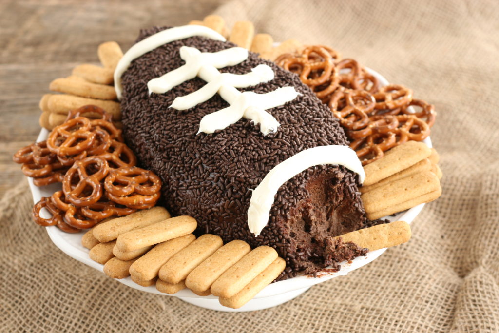 Brownie batter football dip with pretzels and graham cracker sticks with the end of football part way eaten