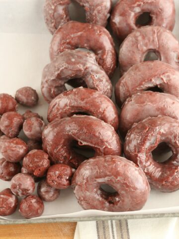 red velvet donuts with glaze lined up against each other in a galvanized tray