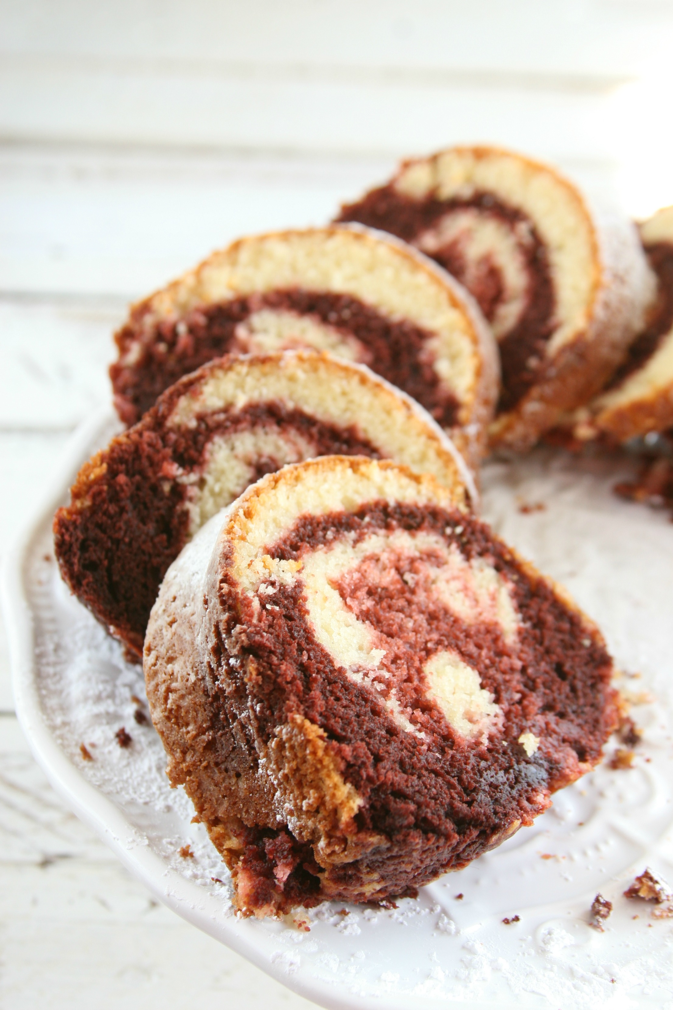 Slices of Red velvet marble Bundt cake on white footed cake dish.