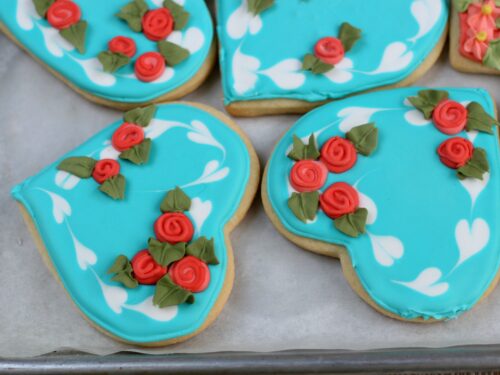 Teal color sugar cookies with red roses and leaf details with royal icing
