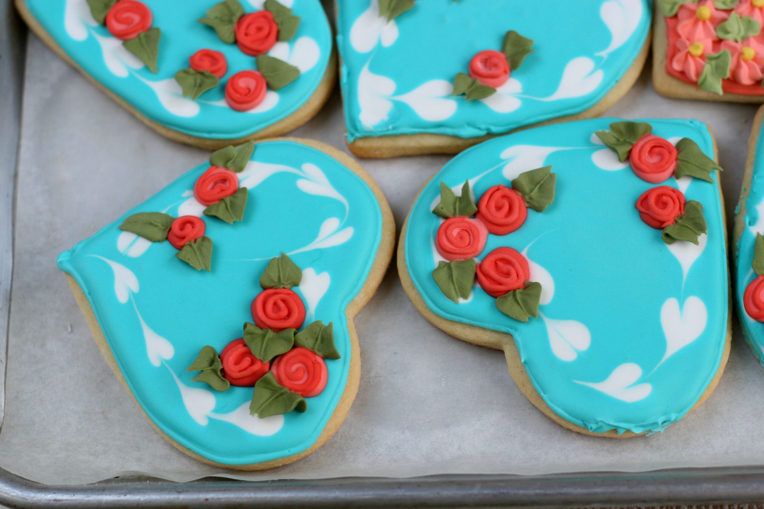 Teal color sugar cookies with red roses and leaf details with royal icing.