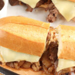 French dip sandwiches cut in half on wooden cutting board.