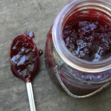 Mixed berry jam in vintage Mason jar and spoonful of jam on old barn wood