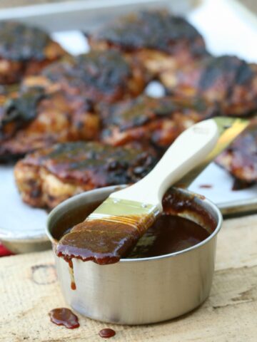 metal measuring cup with barbecue sauce on brush and griled chicken
