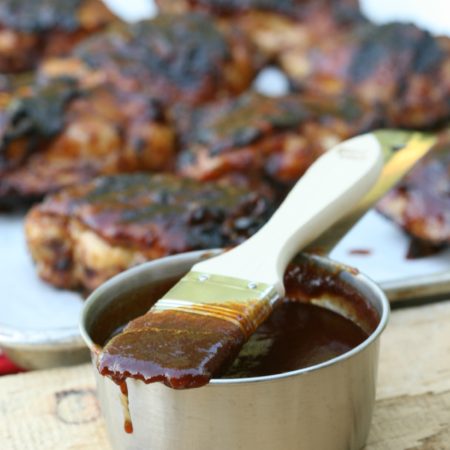 metal measuring cup with barbecue sauce on brush and griled chicken