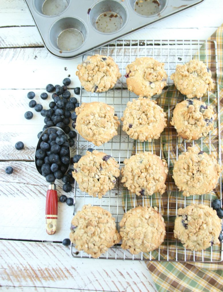 Blueberry muffins cooling on a baking rack, scoop of blueberries on side