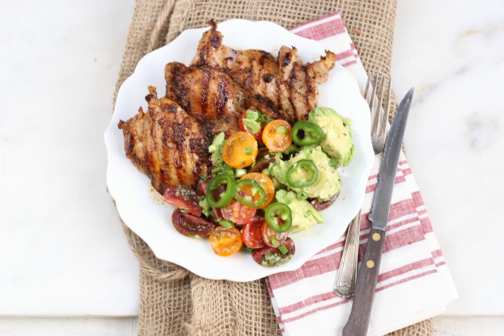 Grilled chicken on white plate with avocado tomato salad with thin slices of jalapenos