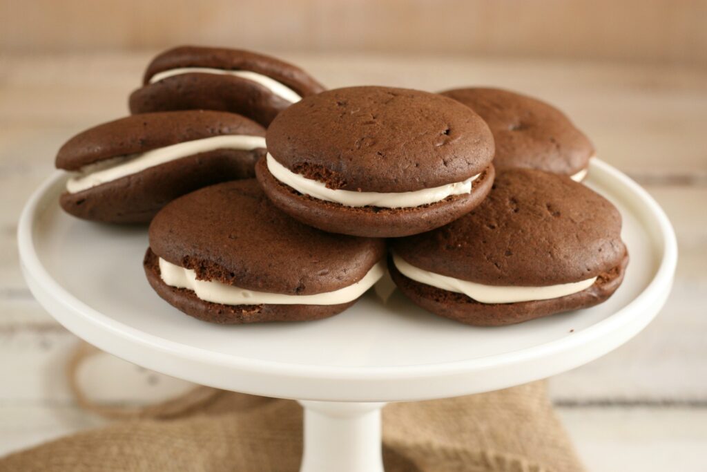 Chocolate Whoopie pies with peanut butter frosting sitting on white glass footed cake dish