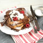 Chocolate brioche french toast on slate cutting board with red and white striped kitchen towel