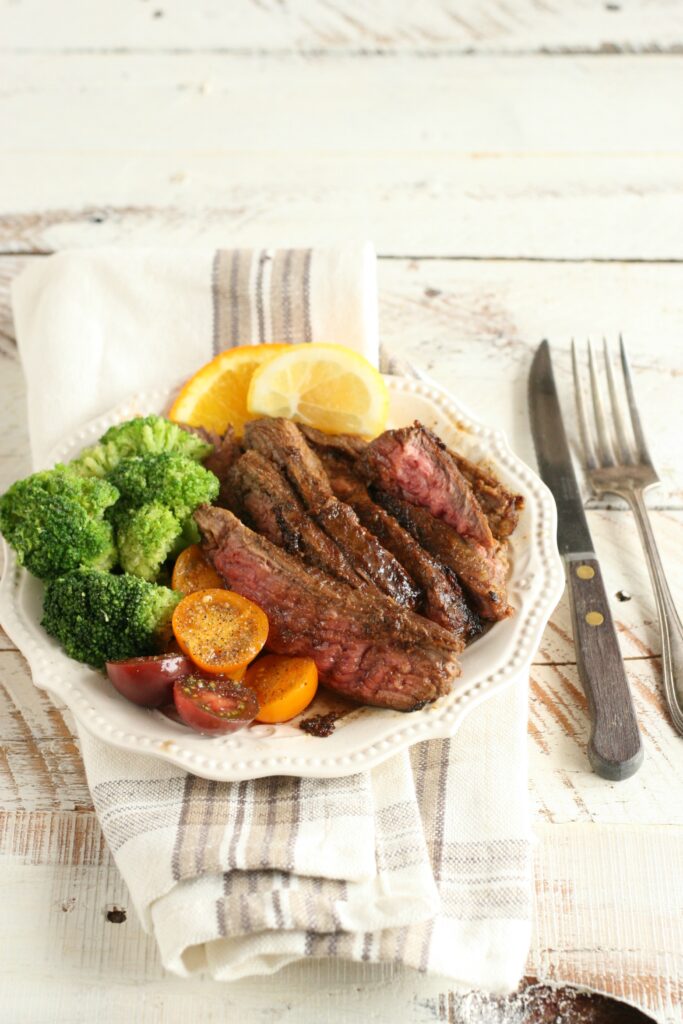 Citrus and Garlic Marinated Flank Steak on a plate with broccoli and cherry tomatoes