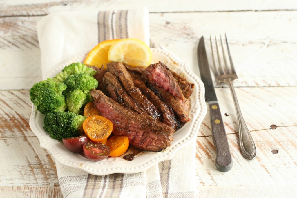 Slices of Citrus and Garlic Marinated Flank Steak on a white plate with broccoli