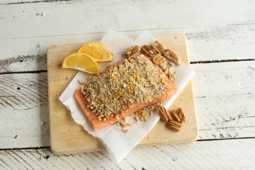 Uncooked Maple Pecan Crusted Salmon on wooden cutting board with pecans and orange slices