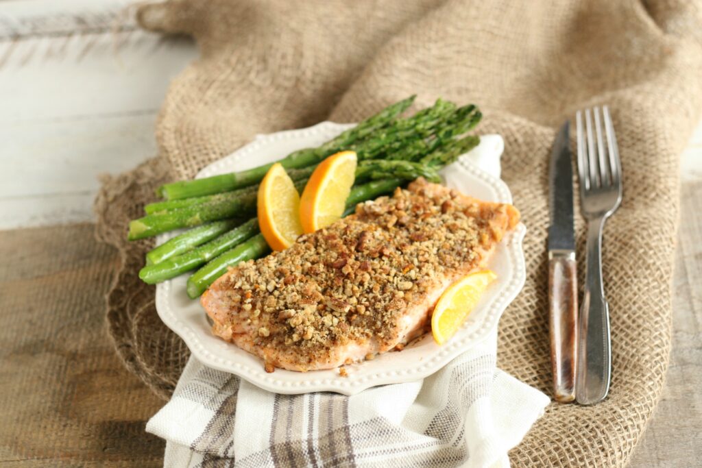 Maple Pecan Crusted Salmon on white plate with asparagus and orange wedges along with knife and fork to the right side of the plate