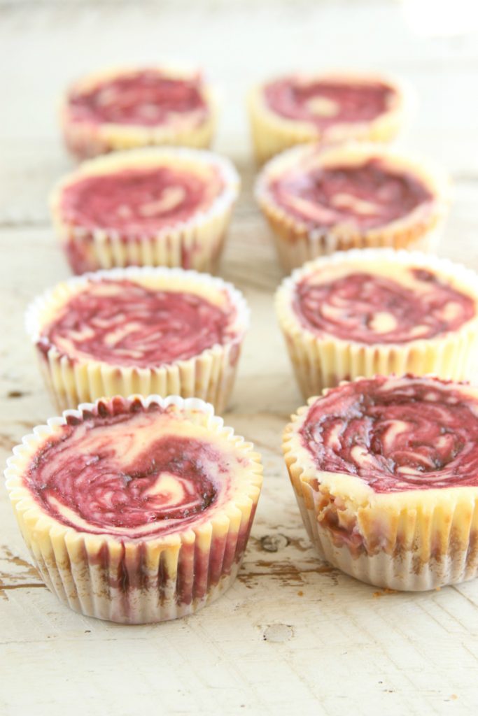 Mini berry swirl cheesecakes lined up on reclaimed wood