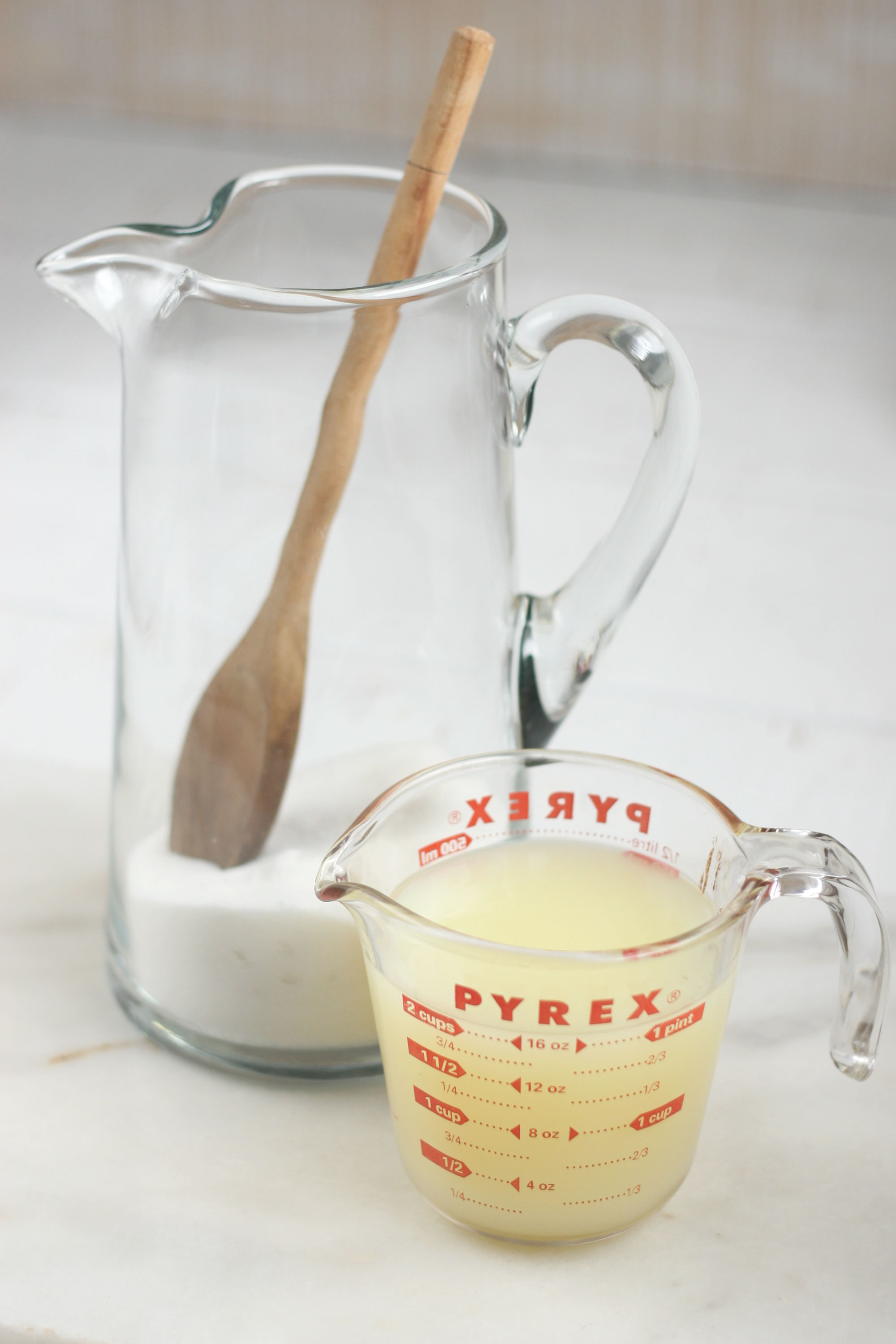 glass pouring pitcher with sugar and measuring cup with lemon juice.