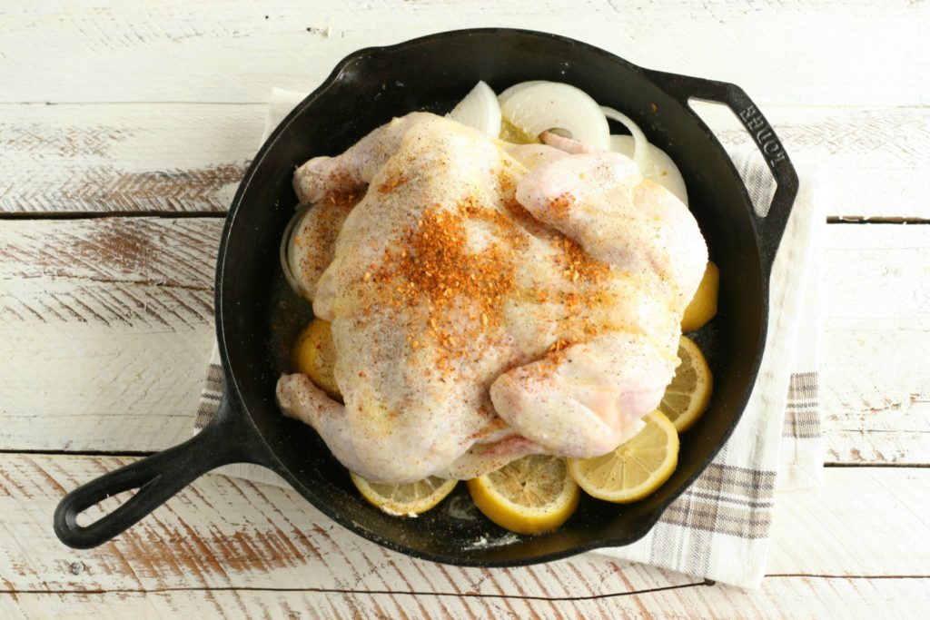 Whole chicken in a cast iron skillet sitting on top of lemon slices