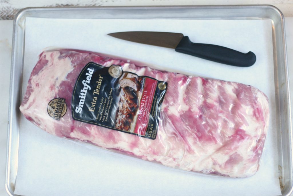 Smithfield All Natural Pork packaged ribs sitting on half sheet pan lined with parchment paper and small chef's knife.