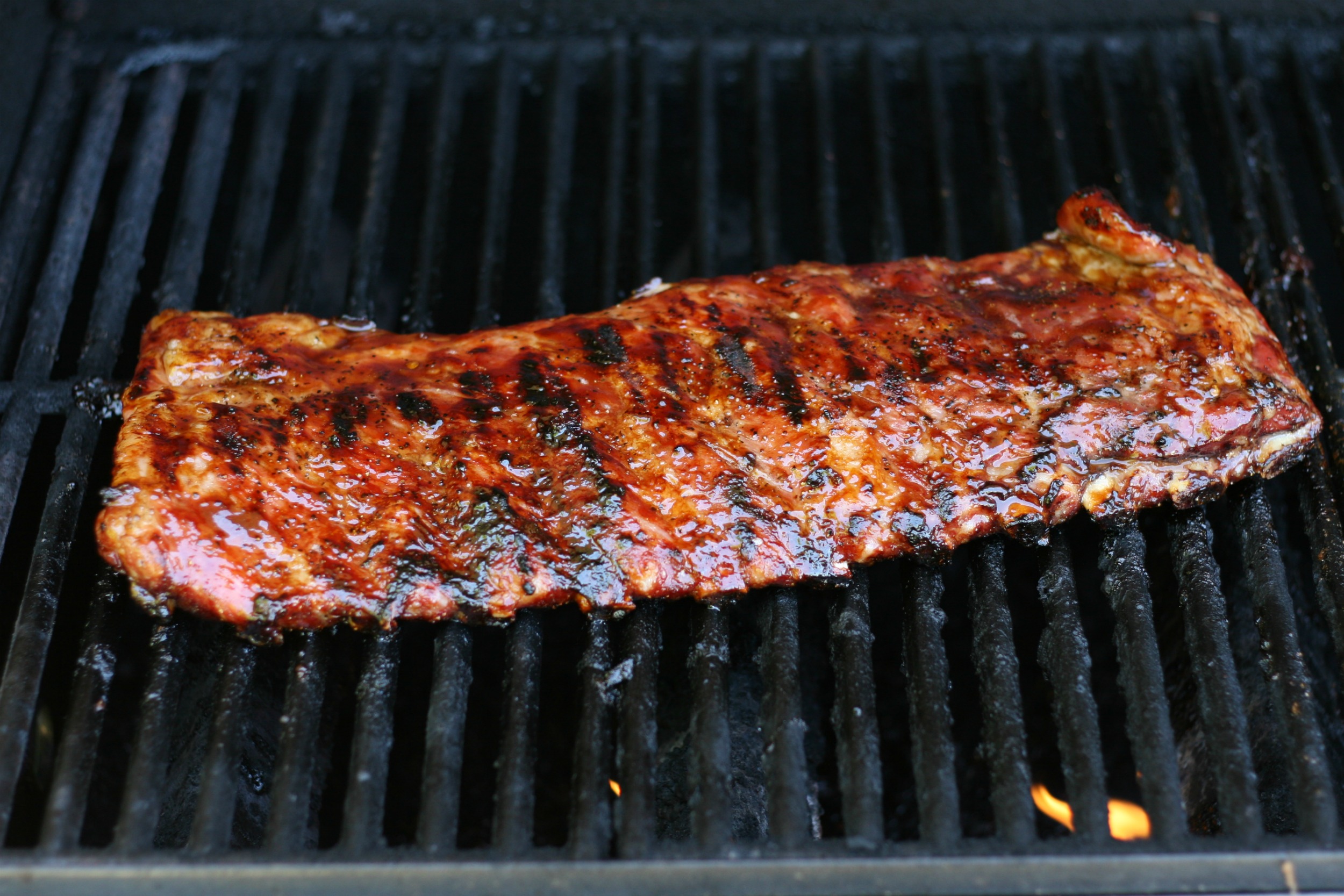 Ribs on grill grates on the gas grill with flames below.