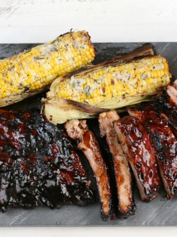 BBQ ribs partially sliced on blue slate and wood tray, corn on the cob.