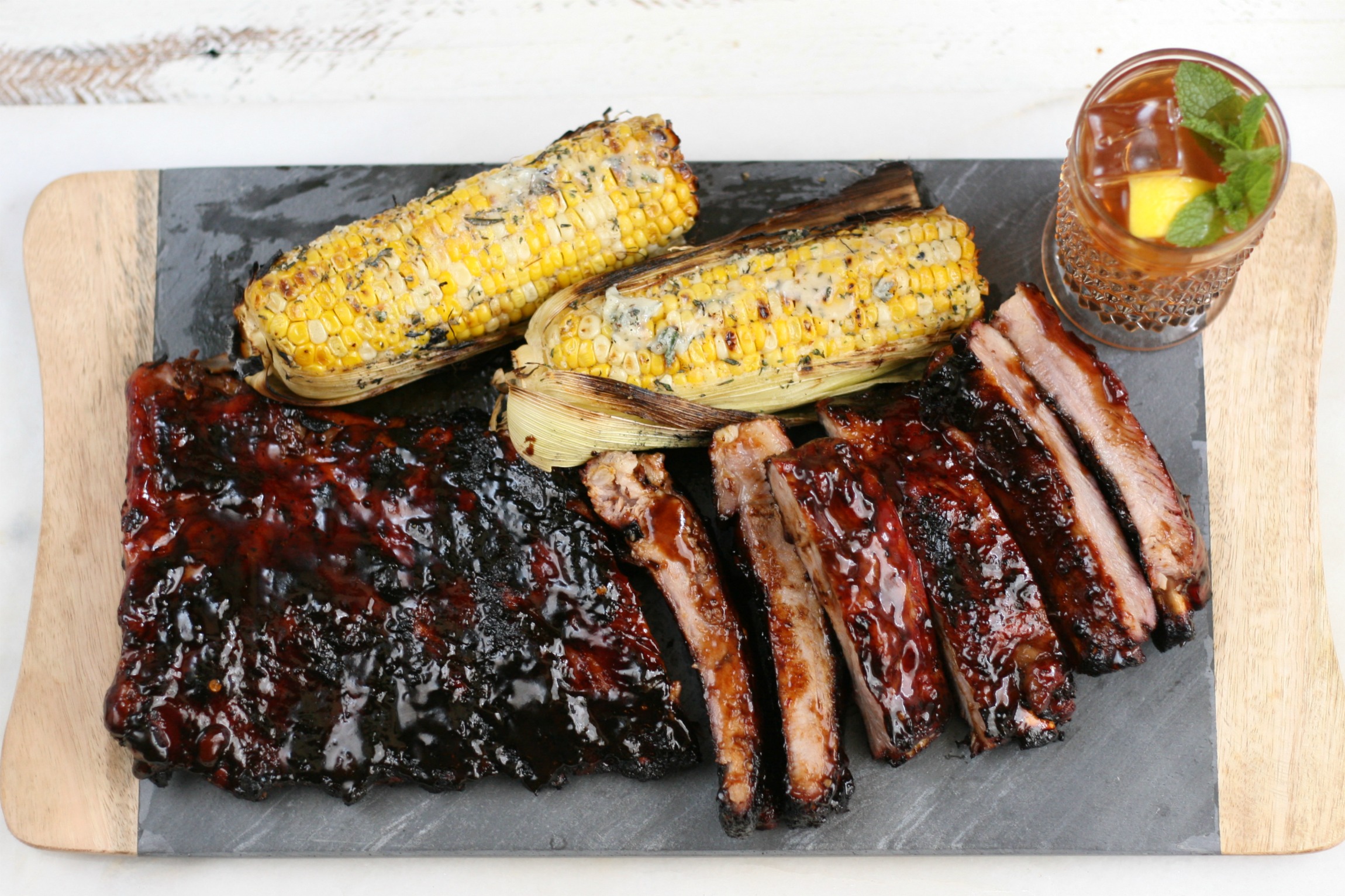BBQ ribs on slate and wood tray, grilled corn on the cob, vintage glass cup of tea.
