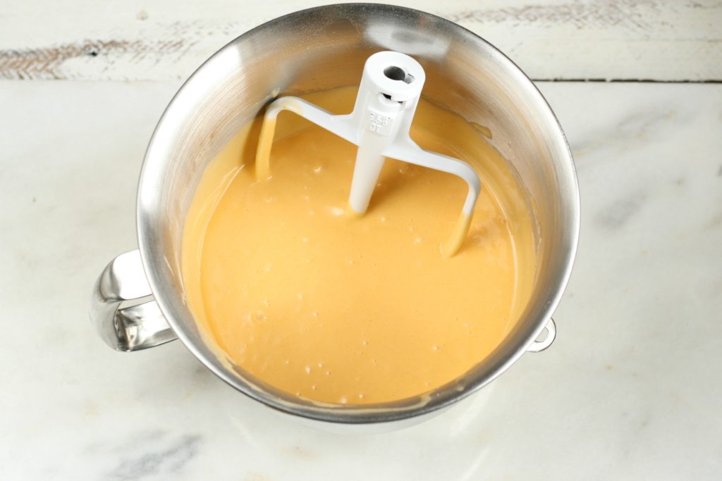 Orange Dreamsicle Cake batter in stand mixer bowl with beater in the batter sitting on a piece of marble