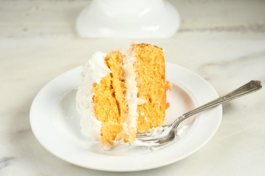 slice of orange dreamsicle cake sitting on a white glass plate with fork on white washed wood